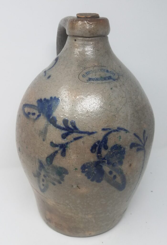 Two-gallon ovoid jug with slip-cup and brush decorated cobalt flower decoratiom. Cobalt-highlighted stamp and cobalt capacity.