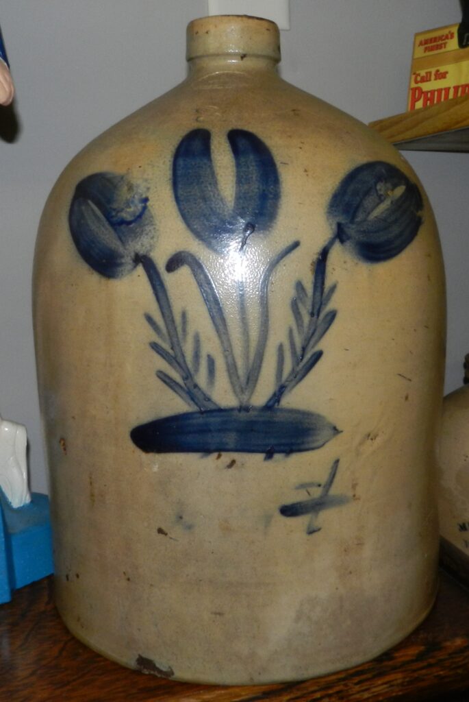Two-gallon salt-glazed handled jug has the Gunther & Berns oval stamp and "2" centered above the flower. It has an exceptional triple flower decoration. that resembles the decoration on a Charles Hermann piece from Milwaukee. Theodore Gunther worked for Hermann for a few years before coming to Sheboygan to partner with Peter Berns. It seems likely that these pieces were  decorated by Th. Gunther.
