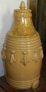 Wheel-thrown barrel-style water dispenser with lid and lead glaze, about six-gallon size with applied decorative medallions and spigot hole. The inside of the lid has a handwritten tally that appears to be the total of the customer’s purchase of four items totaling 80 cents that day. The first item on the list cost 24 cents, probably this five-gallon dispenser, priced at 4 cents per gallon. The three other items were probably also large, priced at 20, 20 and 16 cents each. Prices fell over time from 10 cents per gallon in the 1840’s and 50’s. We attribute this to be from later years of the Depot Pottery, probably the 1870’s or early 1880’s. Private collection.